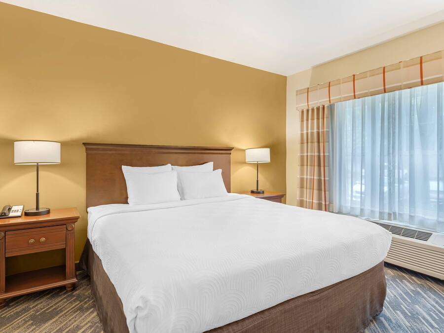 A hotel room with a large bed, two bedside tables with lamps, a telephone, and a window with curtains.
