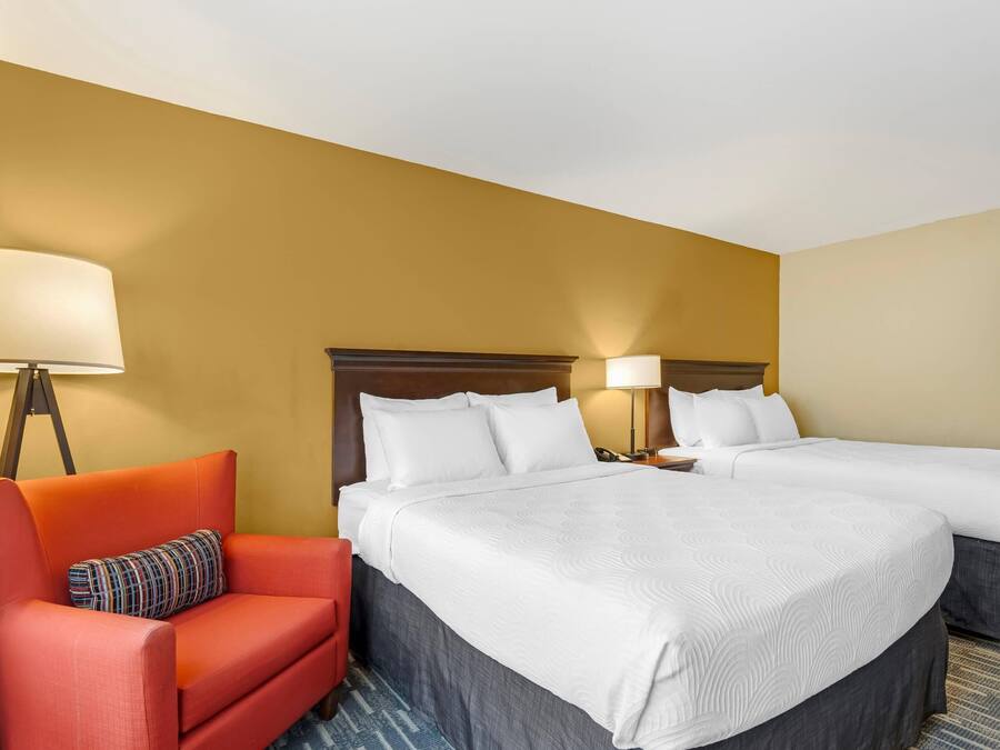 A hotel room with two beds, a red armchair, and a lamp.