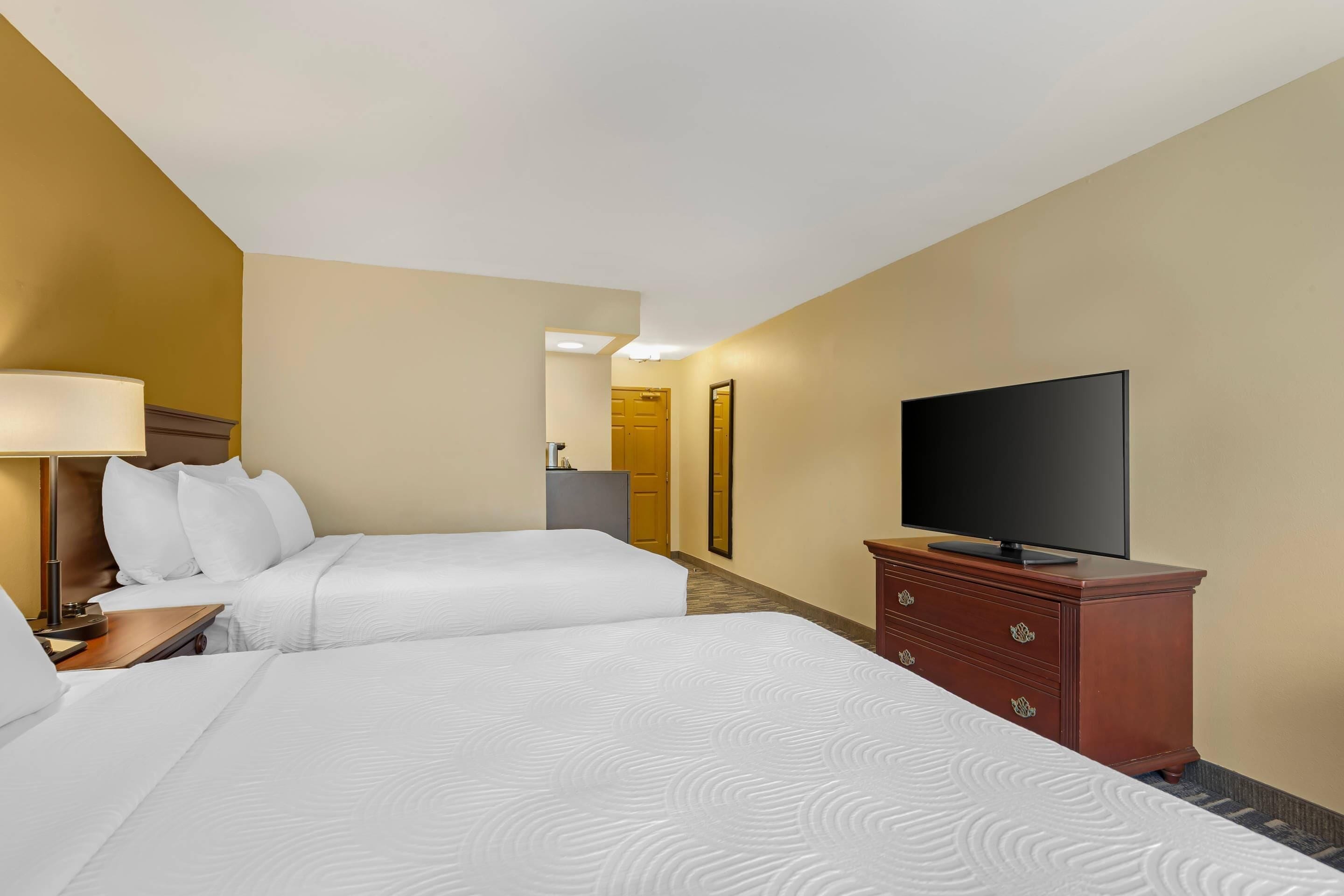 A hotel room with two beds, a television on a dresser, and a desk with a lamp.