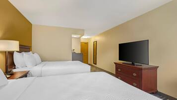 A hotel room with two beds, a television on a dresser, and a desk with a lamp.