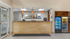 Zona de recepción con mostrador de madera, luces colgantes, cuadros en la pared y un refrigerador lleno de bebidas.