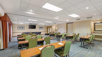 A conference room with multiple tables and chairs, equipped with water bottles, and a projector screen on the wall.