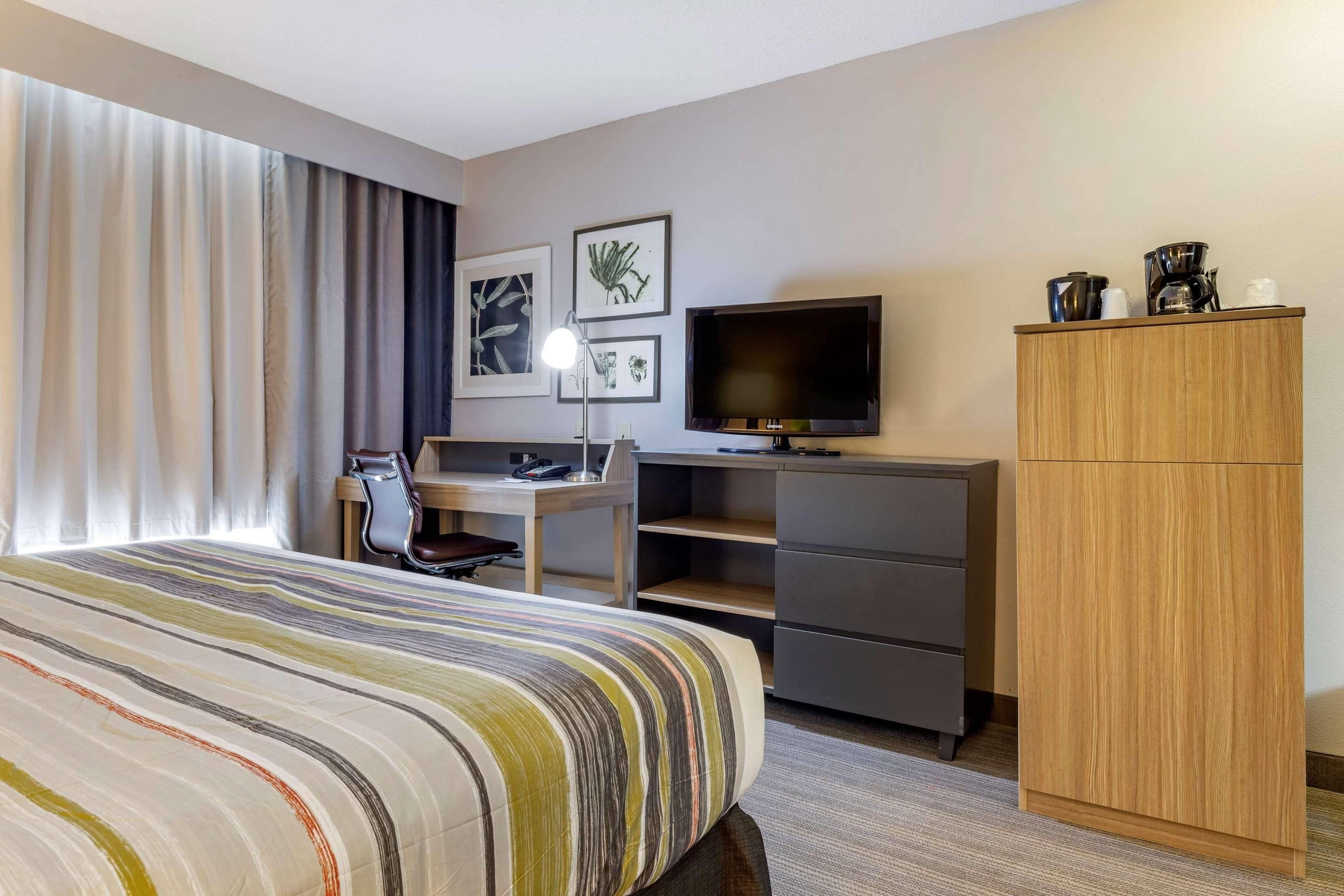Una habitación de hotel con cama, escritorio, televisor y armario.