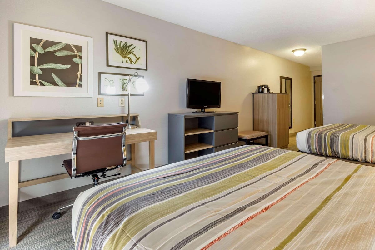 A hotel room with a bed, a desk with a chair, a television, and artwork on the walls.