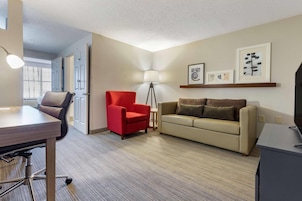 Un salón moderno con un escritorio, un sillón rojo, un sofá color beige y una lámpara de pie.