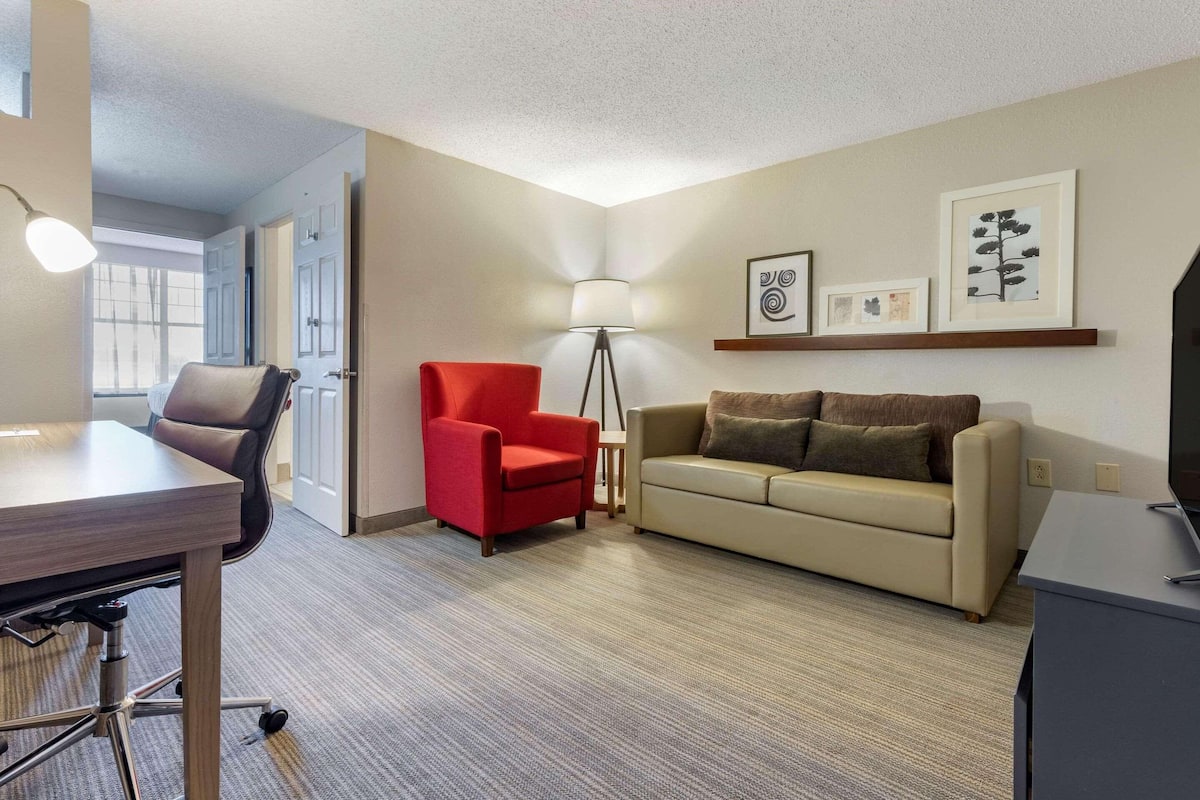 A modern living room with a desk, a red chair, a beige sofa, and a floor lamp.