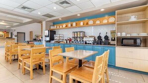 A modern restaurant with wooden tables and chairs, a kitchen area with blue cabinets, and a variety of dishes displayed on shelves. - Country Inn & Suites by Radisson, Lumberton, NC (Lumberton)