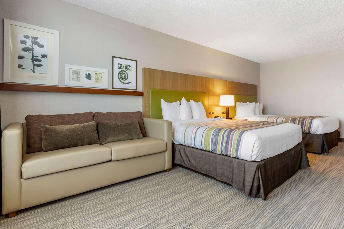 A hotel room with a sofa, two beds, and framed artwork on the wall.