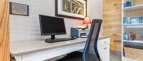 Ett hotellrum med ett skrivbord, en dator, en stol och en bokhylla.