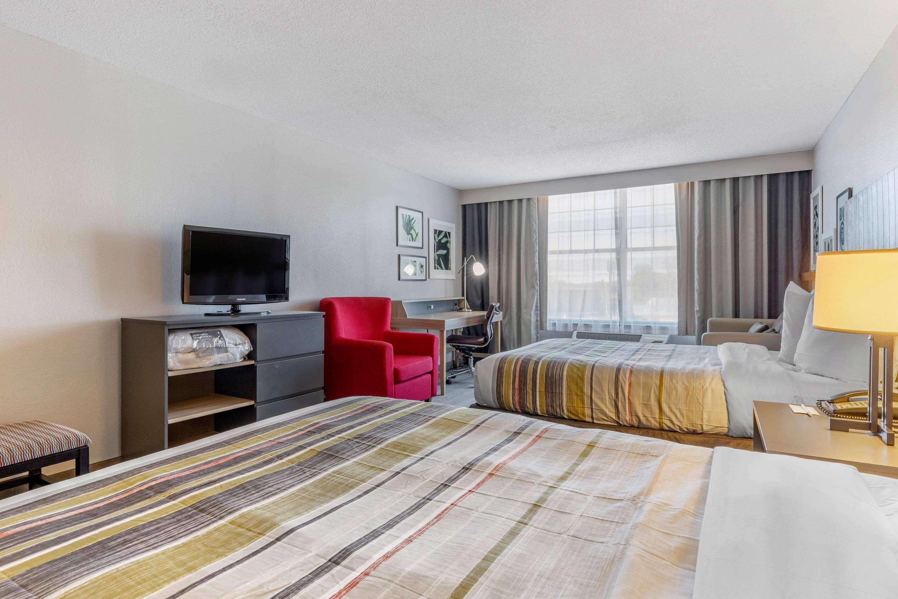 A hotel room with two beds, a desk, a chair, a television, and a window with curtains.