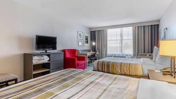 A hotel room with two beds, a desk, a chair, a television, and a window with curtains.