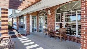 A covered outdoor seating area with brick walls, wooden furniture, and large windows. - Country Inn & Suites by Radisson, Lumberton, NC (Lumberton)
