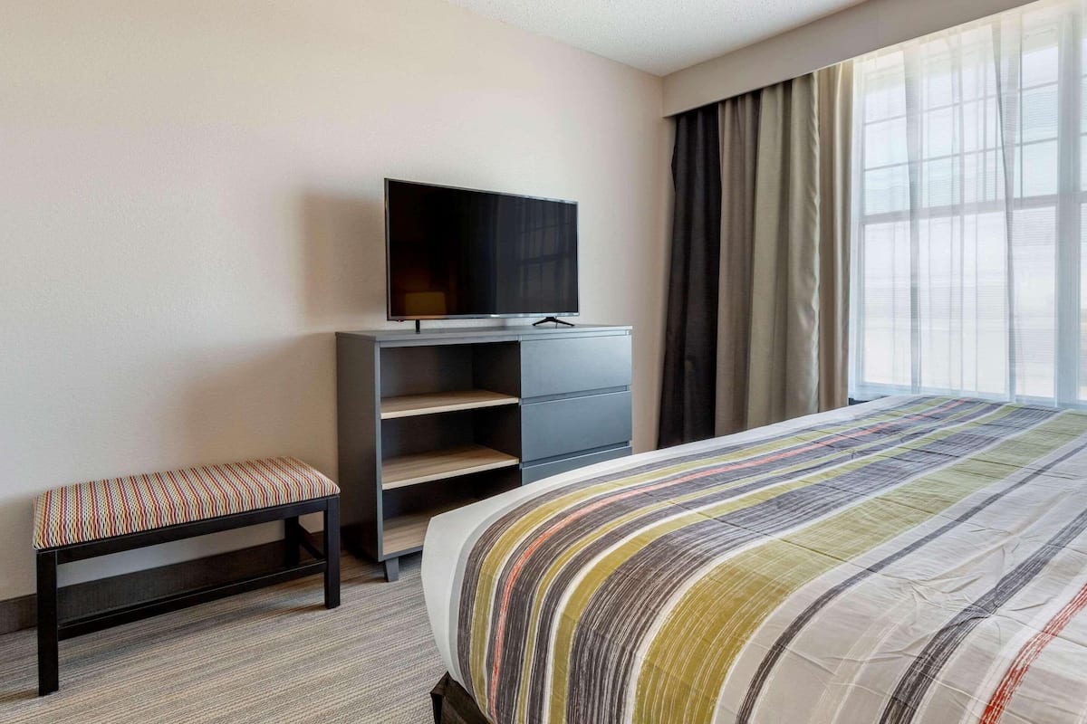 A hotel room with a bed, a bench, a TV on a stand, a wardrobe, and a window with curtains.