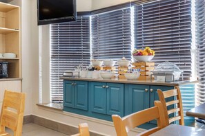 A kitchen with teal cabinets, a dining table, and chairs. There are bowls and a fruit bowl on the counter.