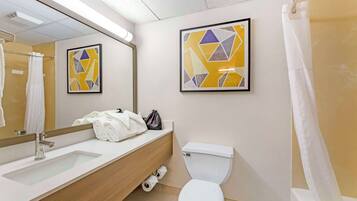 A modern bathroom with a sink, toilet, and shower. There are towels and a bag on the counter.