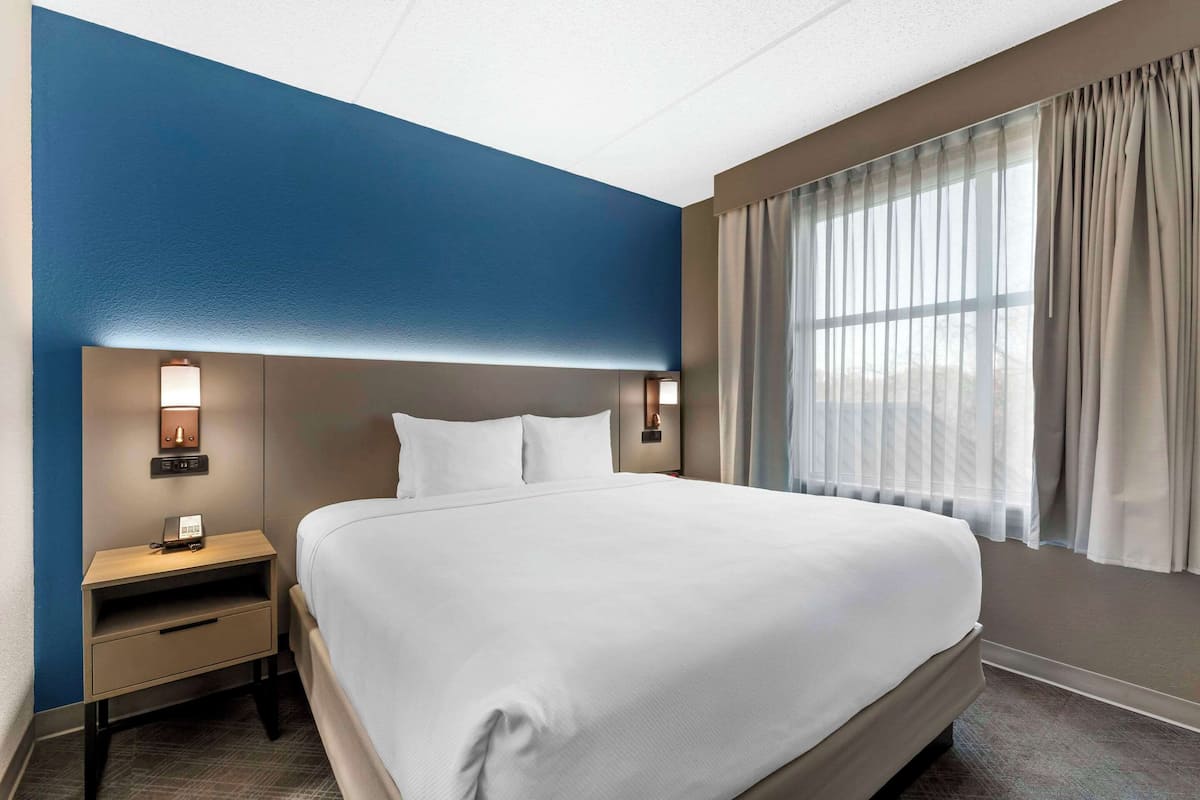 A hotel room with a large bed, a nightstand with a lamp, and a window with curtains.