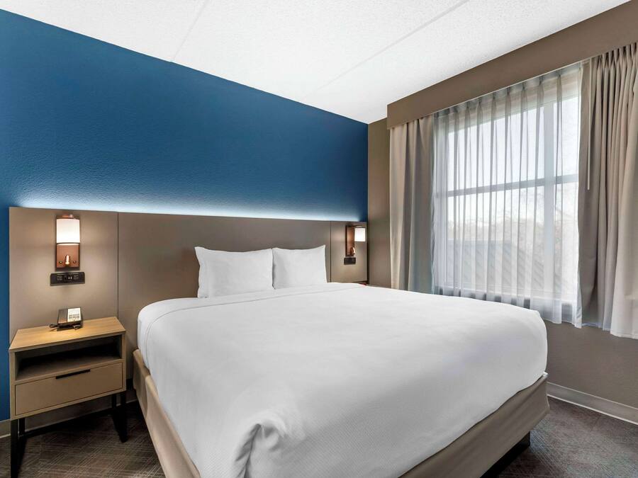 Una habitación de hotel con una cama grande, una mesita de noche con lámpara y una ventana con cortinas.