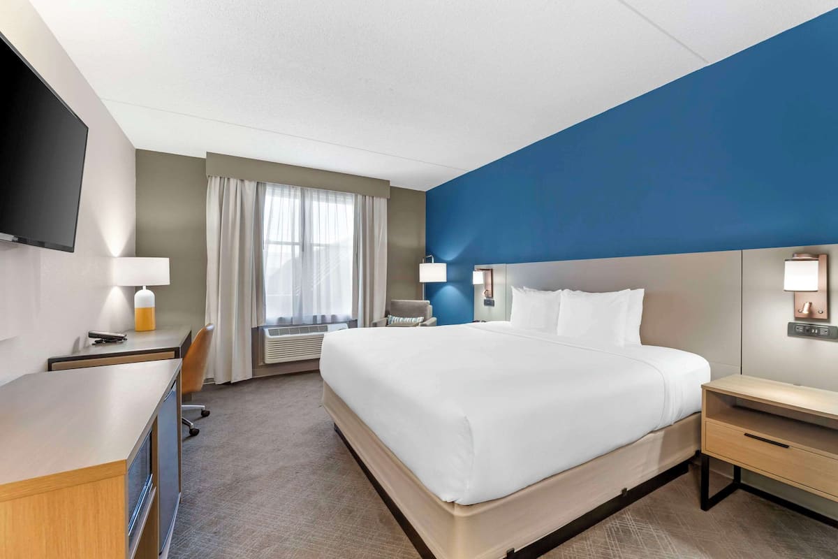 A hotel room with a large bed, a desk, a chair, a TV, and a window with curtains.