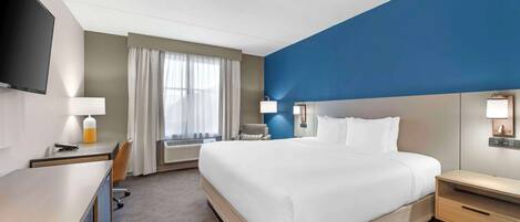 A hotel room with a large bed, a desk, a chair, a TV, and a window with curtains.