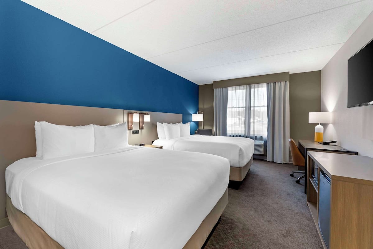 A hotel room with two beds, a desk, a chair, and a TV.