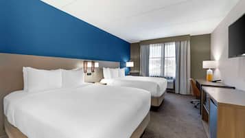A hotel room with two beds, a desk, a chair, and a TV.