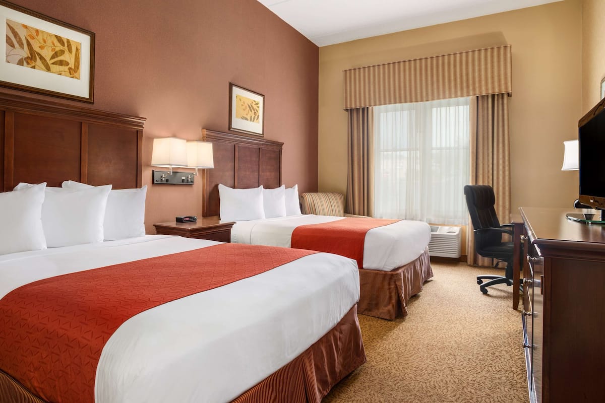 A hotel room with two beds, a desk, a chair, a lamp, and a large window with curtains.