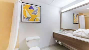 Un baño moderno con inodoro, lavamanos y ducha. Hay dos cuadros abstractos enmarcados en la pared.