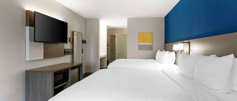 A hotel room with a large bed, a flat-screen TV mounted on the wall, a desk with a microwave, and a small cabinet.