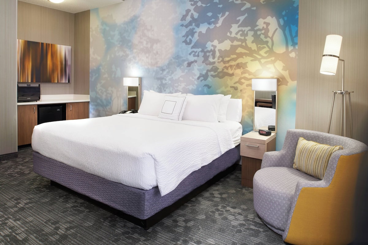 Ein modernes Hotelzimmer mit einem großen Bett, zwei Nachttischen, einem Flachbildfernseher, einem Schreibtisch und einem Sessel.
