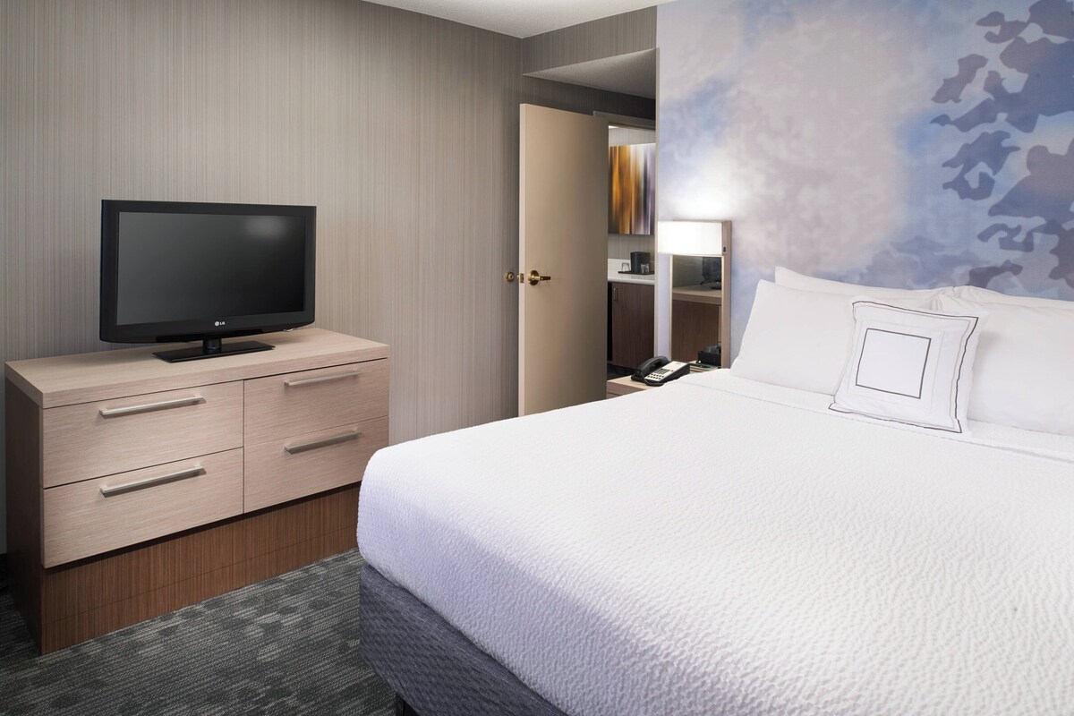 A hotel room with a bed, a TV on a wooden dresser, a phone, and a door leading to a bathroom.