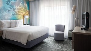 A hotel room with a large bed, a desk with a television, a chair, and a window with curtains. - Courtyard by Marriott Toledo Maumee/Arrowhead (Maumee)