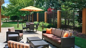 An outdoor patio area with wicker furniture, a table, and an umbrella. - Courtyard by Marriott Toledo Maumee/Arrowhead (Maumee)