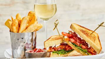 Une assiette avec un sandwich grillé, un verre de vin blanc et une tasse en métal remplie de frites.