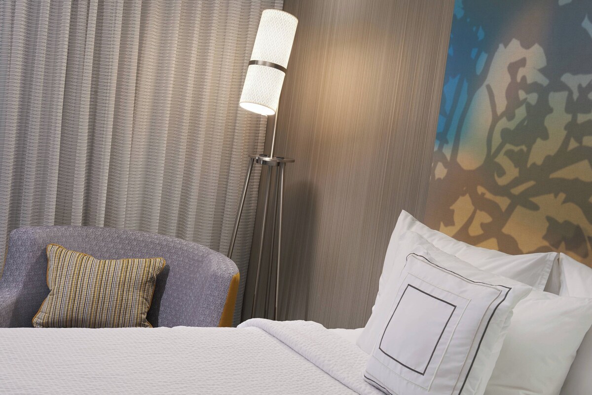A hotel room with a bed, a standing floor lamp, and a patterned wall.