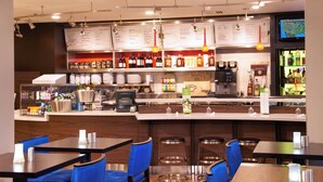 A restaurant with a bar area, blue chairs, and a menu board. - Courtyard by Marriott Toledo Maumee/Arrowhead (Maumee)