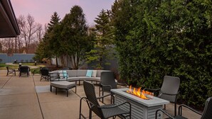 Une terrasse extérieure dotée d’un foyer, d’un espace salon et offrant une vue sur les arbres et les bâtiments environnants.