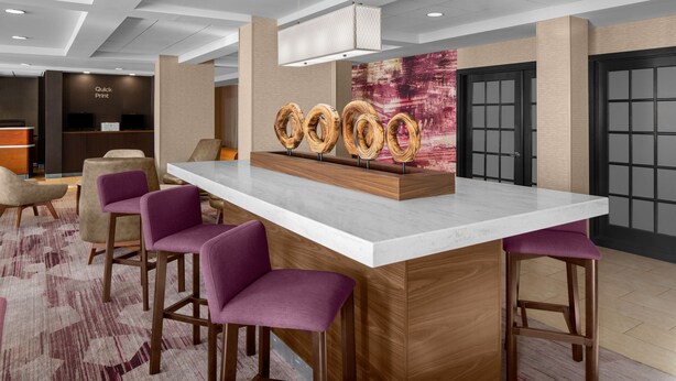 Un espace bar moderne doté d’un comptoir en marbre, de tabourets en bois et d’un présentoir décoratif en forme d’anneau en bois.