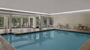 Une piscine entourée de grandes baies vitrées, avec des chaises longues et des tables à proximité.