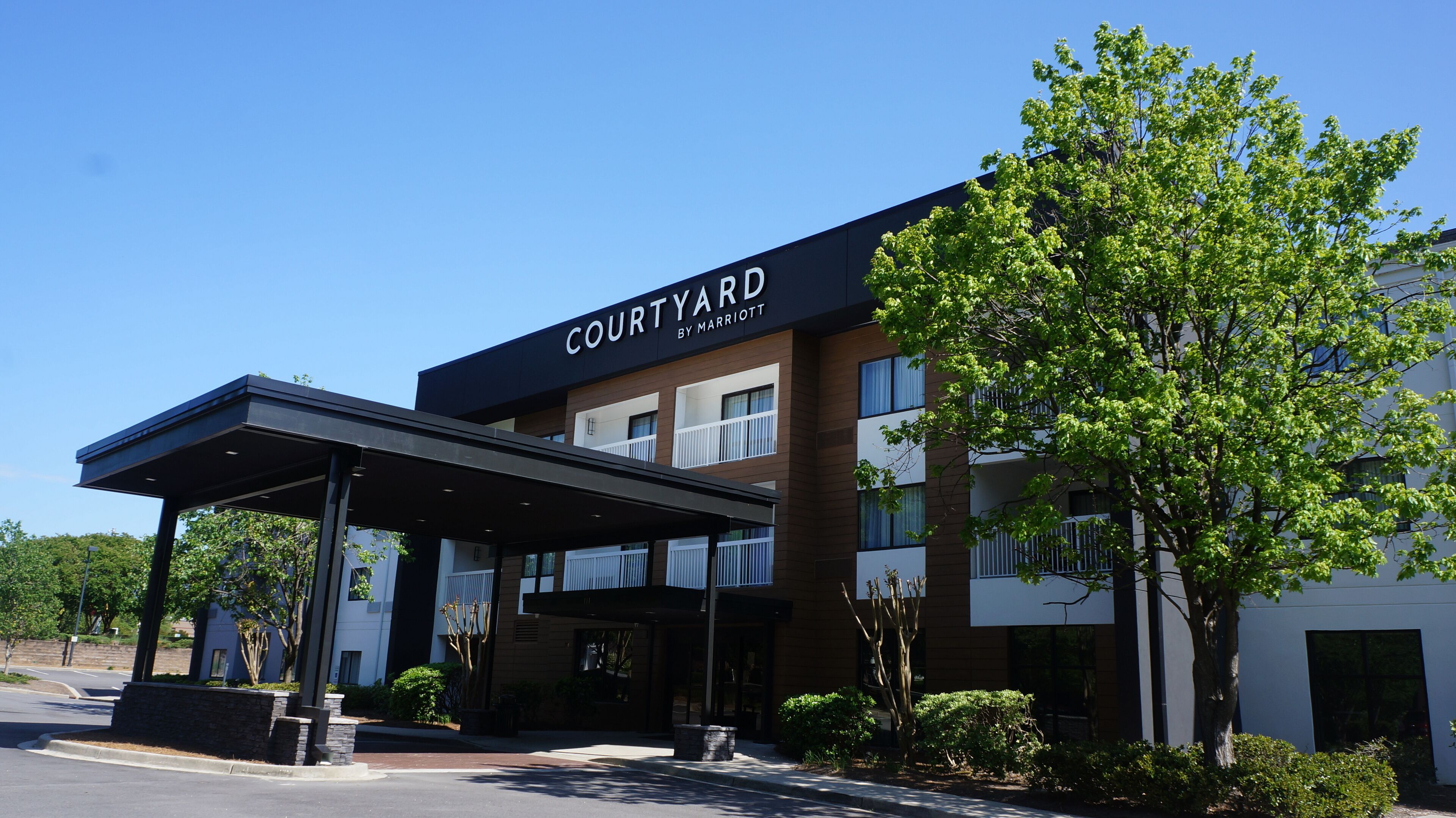 Een Courtyard by Marriott hotel met een overdekte ingang, meerdere balkons en weelderige begroeiing.
