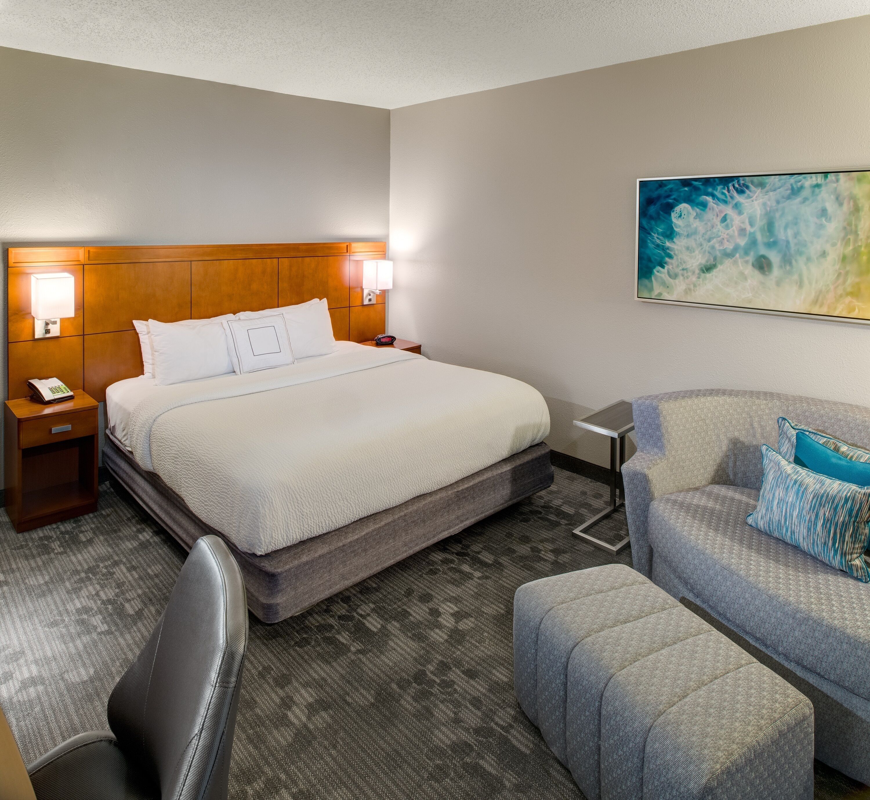 Quarto de hotel com cama, abajures, escrivaninha, cadeira e sofá.
