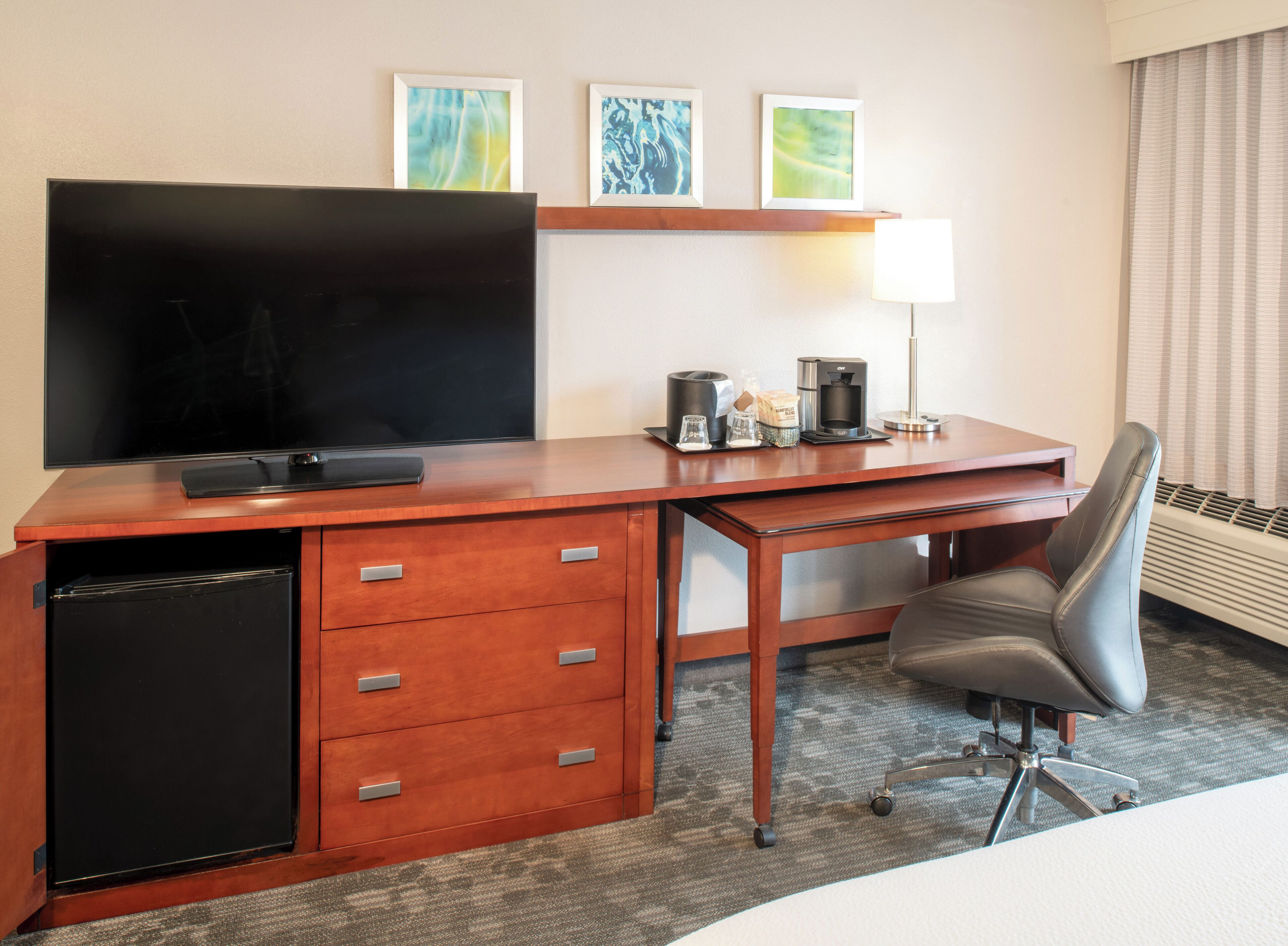 A hotel room with a wooden desk, a television, a coffee maker, and a chair.