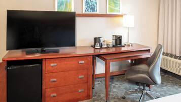 A hotel room with a wooden desk, a television, a coffee maker, and a chair.