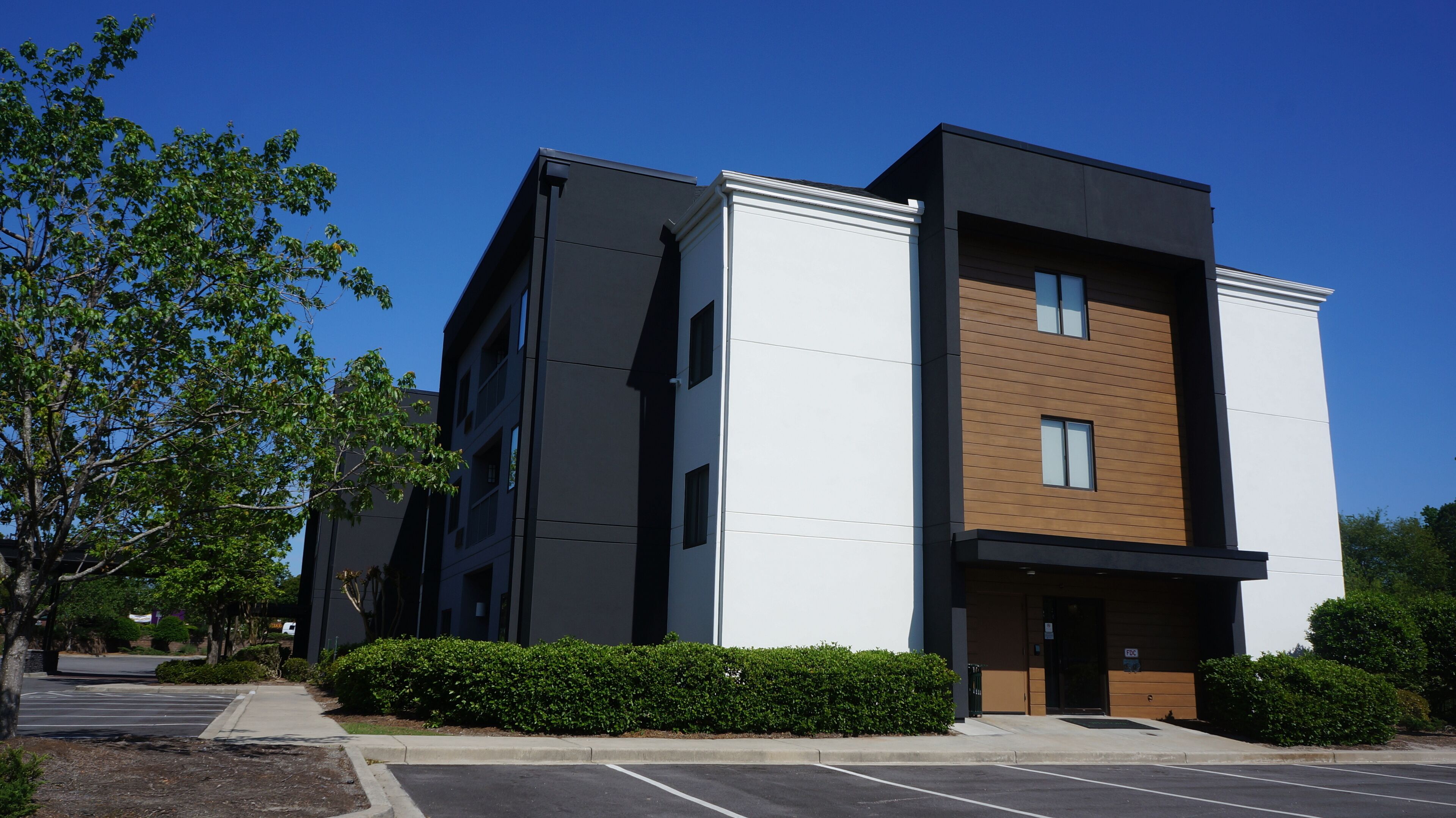 A modern multi-story building with a flat roof, large windows, and a parking lot.