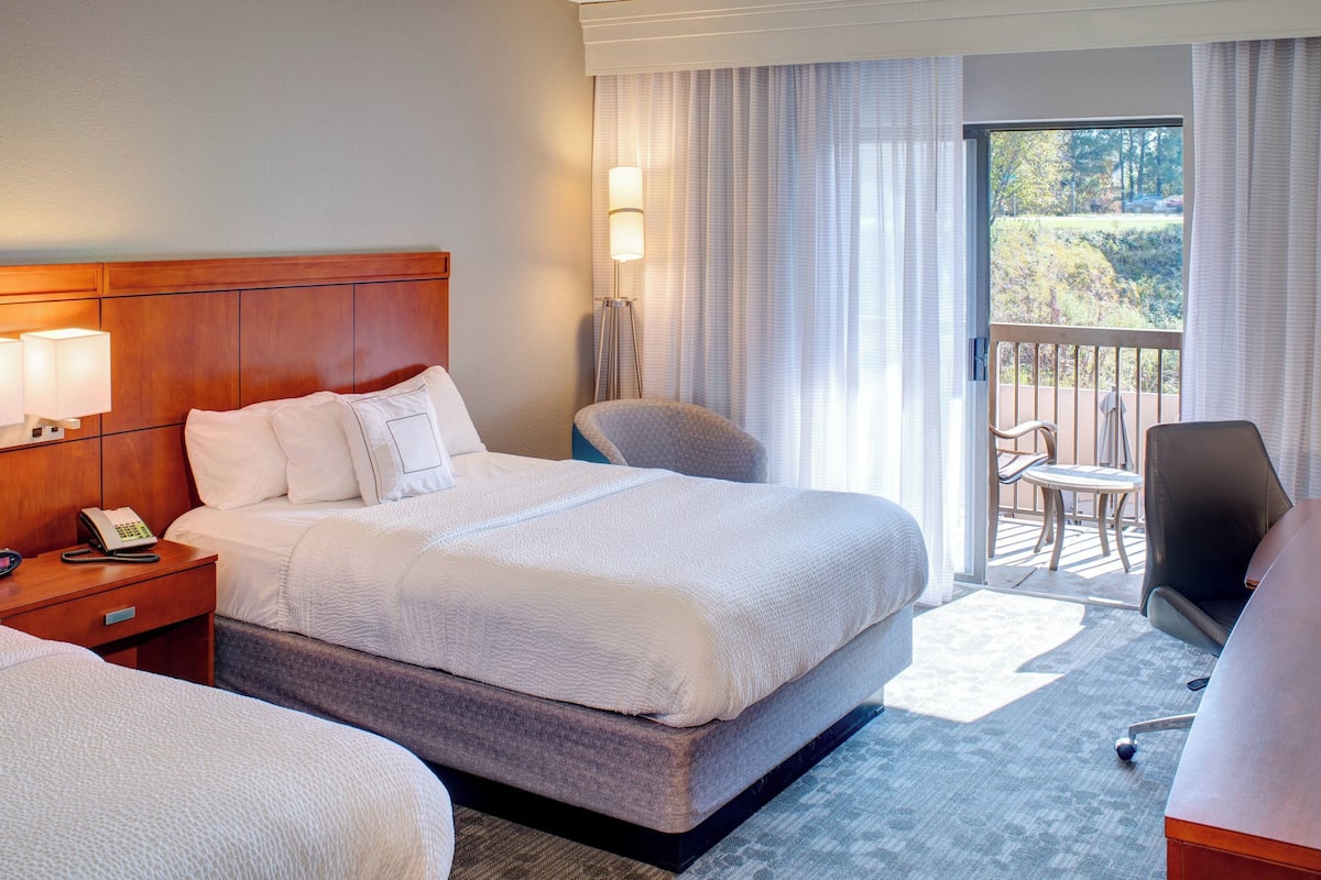 Une chambre d’hôtel avec un grand lit, une table de chevet avec une lampe, une chaise et une vue sur l’extérieur grâce à une porte coulissante.