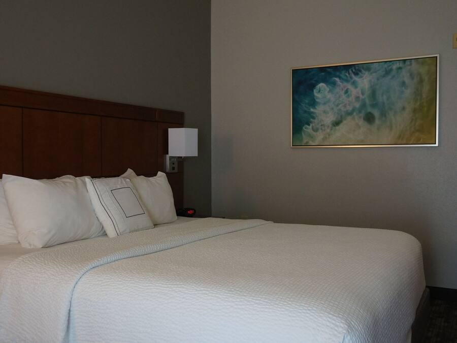 A hotel room with a large bed, a wooden headboard, a nightstand, a bedside lamp, and a painting on the wall.