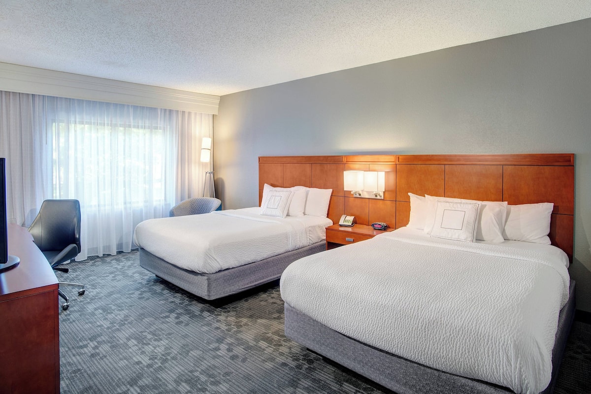 Une chambre d’hôtel avec deux lits, un bureau, une chaise et un téléviseur.