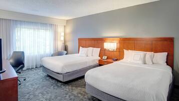 A hotel room with two beds, a desk, a chair, and a TV.