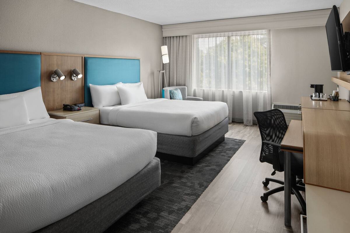 A hotel room with two beds, a desk, a chair, a TV, and a window with curtains.
