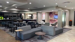 Un moderno vestíbulo de hotel con una zona de bar, arreglos para sentarse y una pantalla grande que muestra un programa.