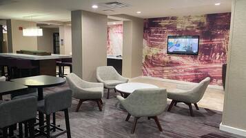 Un área de descanso moderna con bar, asientos y una pantalla de televisión en la pared.
